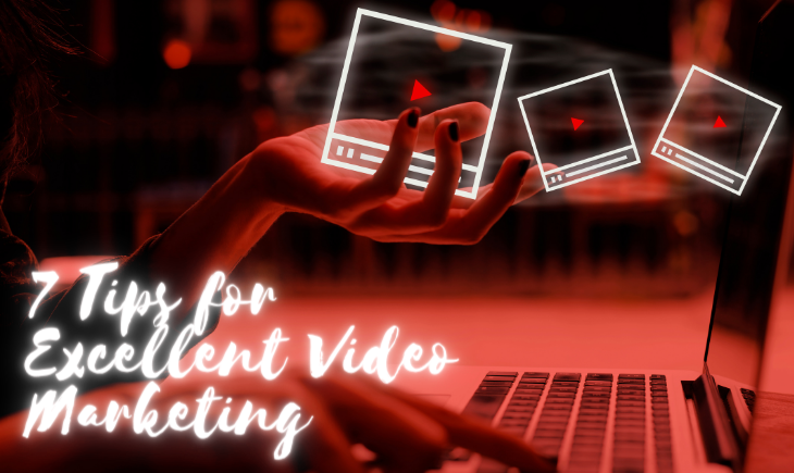 An unseen woman is on her laptop typing with her right hand and holding up a graphic of videos with her left. The room is cast in a red light. The title of the article, "7 Tips for Excellent Video Marketing," is written in white in the bottom-left corner.